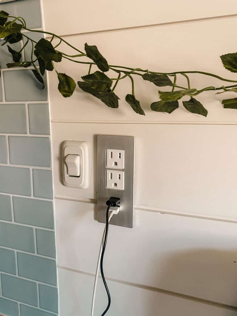 A silver and white outlet that is part of a camper van electrical system is on the van's wall, next to a white light switch.