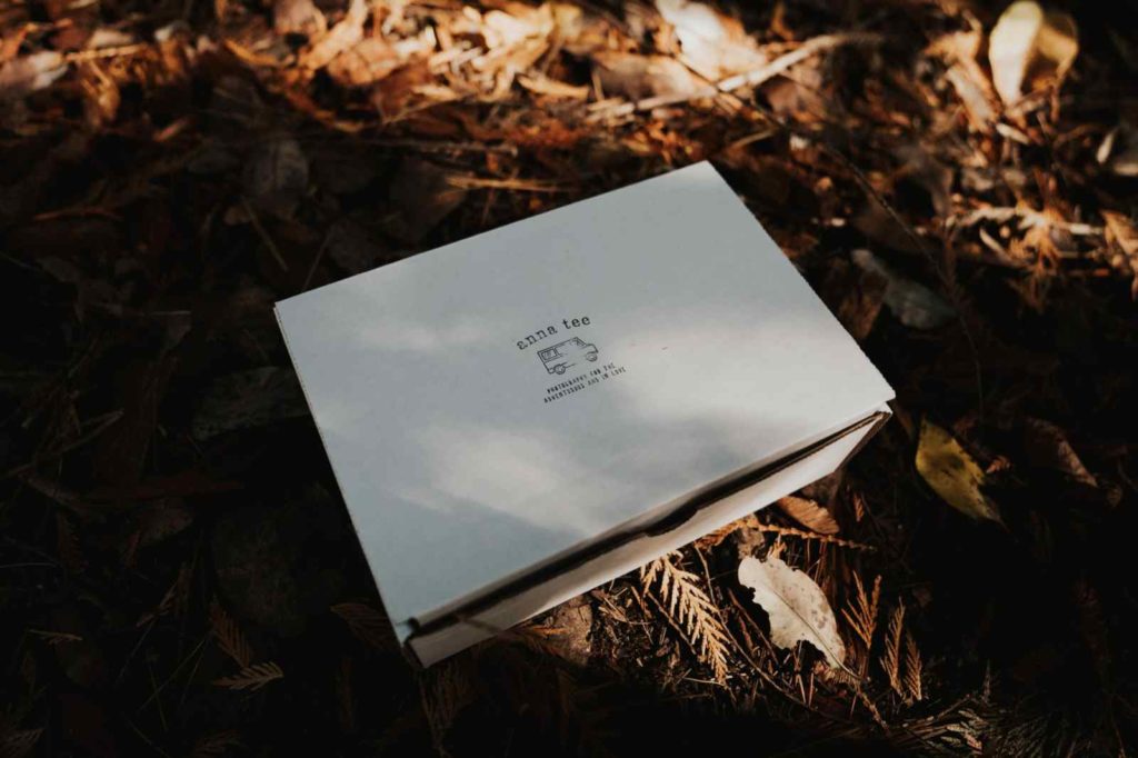 A white wedding photography client gift box is lying on the ground, on top of some brown leaves.