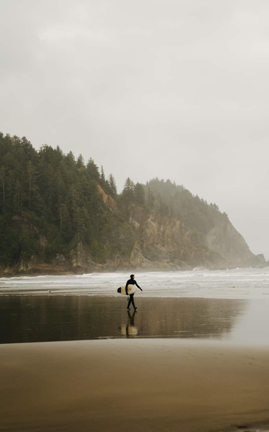 A surfer at Short Sands Beach is walking into the ocean water.