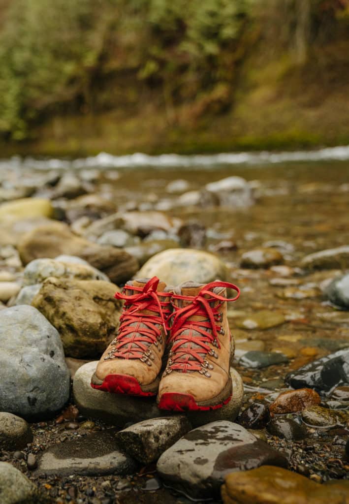 A pair of Danner Mountiain 600 boots are on top of a rock in front of a river.