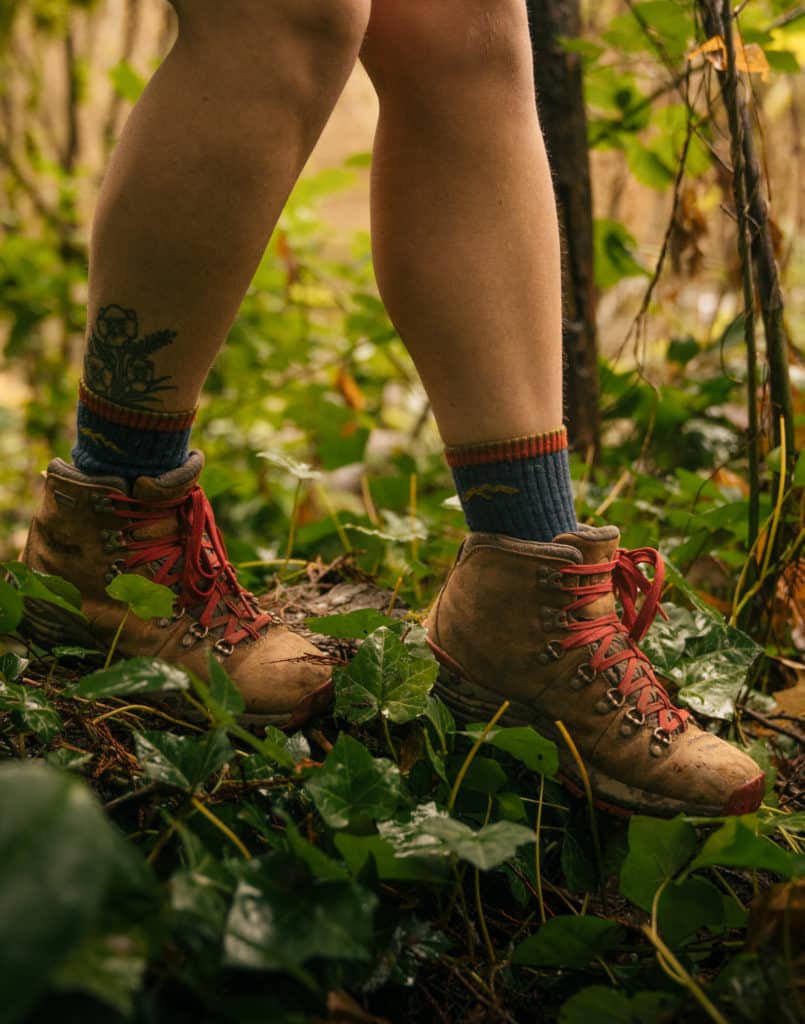 A closeup of the Danner Mountain 600 boots, as a person steps off of a log onto a grassy field.