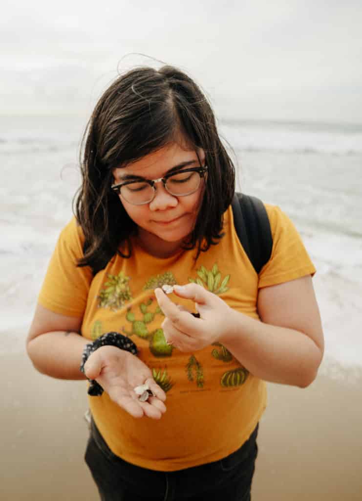 A girl in a bright yellow shirt is looking at a seashell at the Sunset Cliffs Natural Park beach.