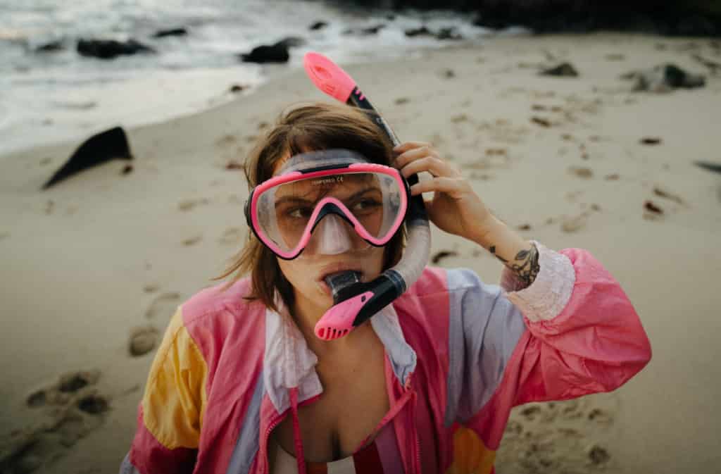 A girl is standing on the beach at La Jolla Cove, with a pink snorkel and mask on.