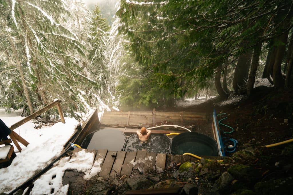 Scenic Hot Springs from above, with three tubs surrounded by a forested landscape and snow.