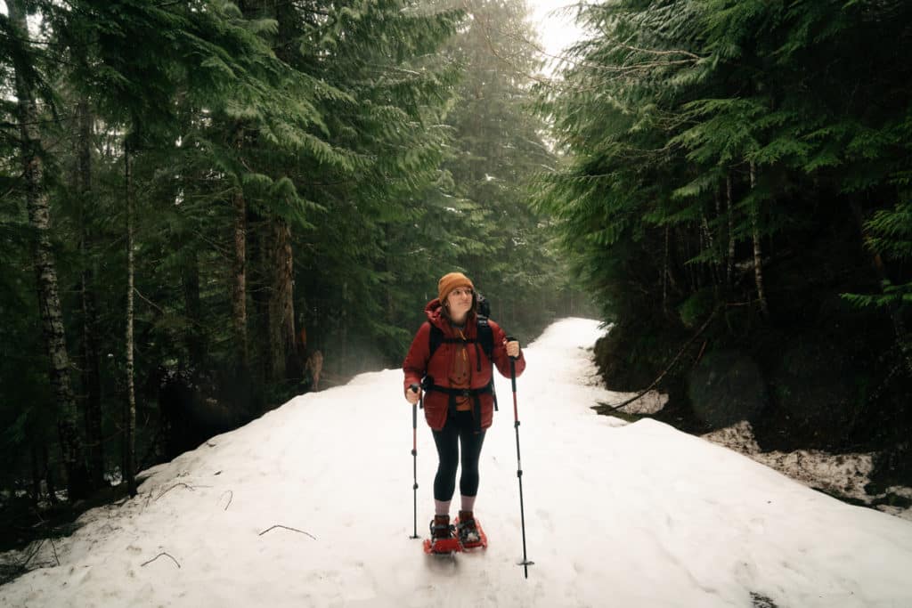 A girl wearing a red jacket is snowshoeing on the trail to Scenic Hot Springs, with snow on the ground and trees surrounding the trail.
