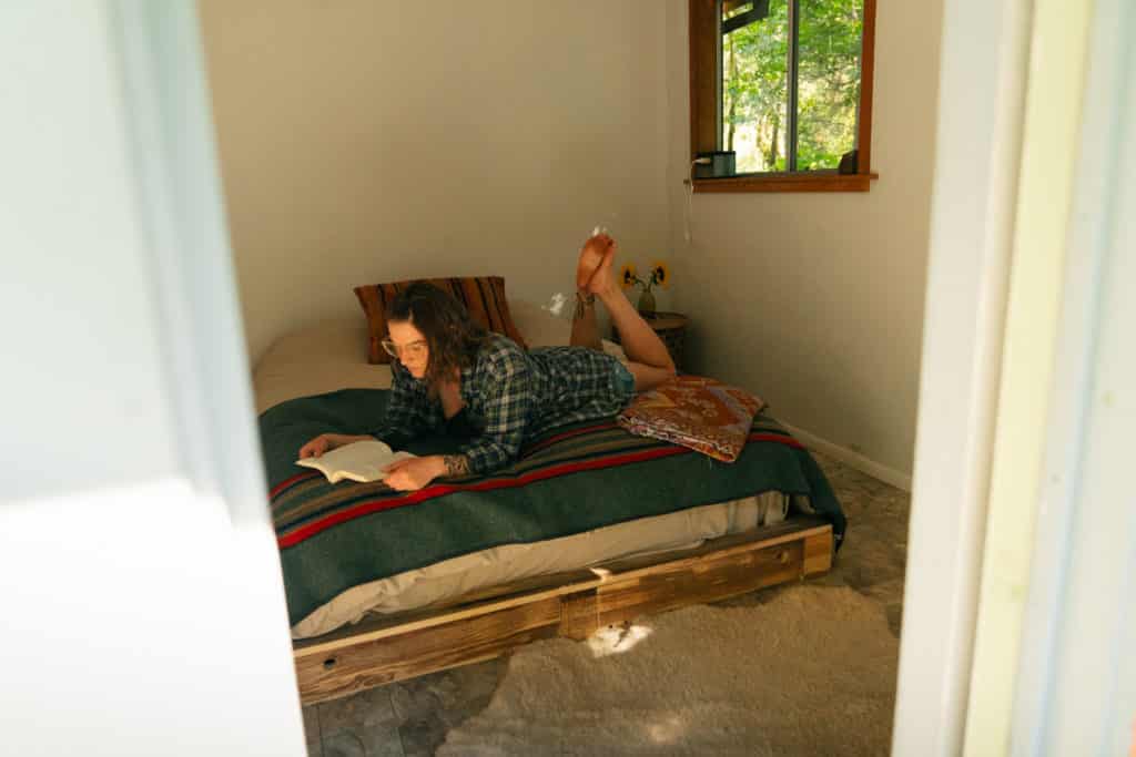 Me laying on the bed inside a cabin in the redwoods, reading a book.