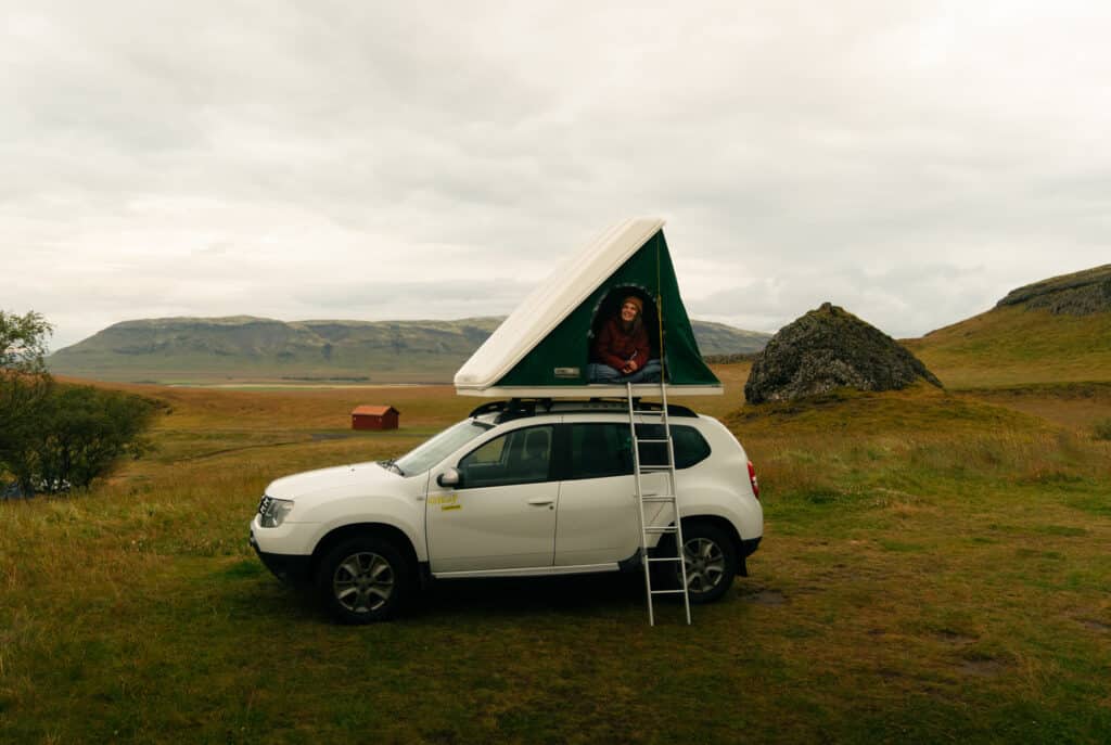 Me sitting in the rooftop tent of my rental car, car camping at one of the best campsites in Iceland!