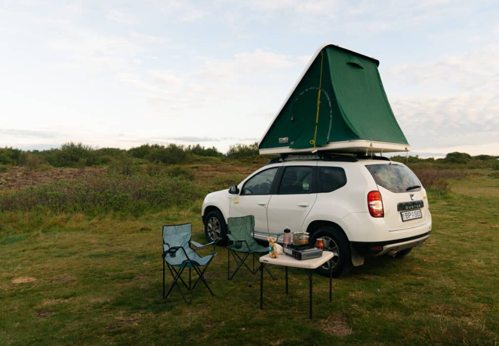A view of our car camping setup in Iceland, with a rooftop tent, and tables and chairs outside.