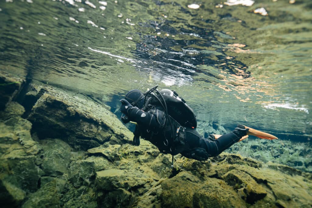 A scuba diver swimming over a rock wall in the Silfra Fissure.
