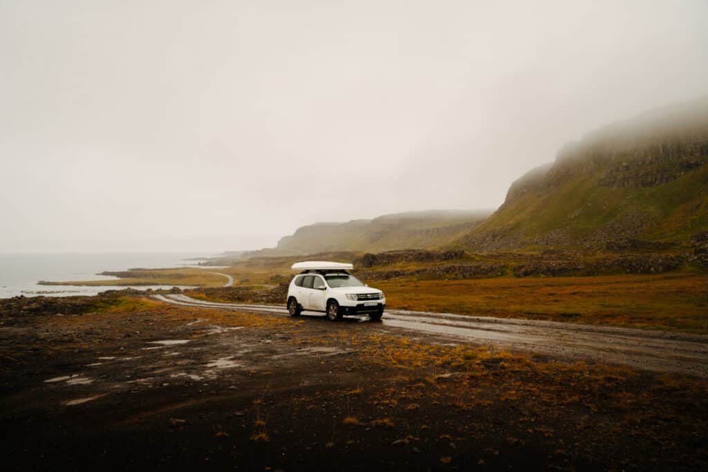 A car stopped on the Ring Road in Iceland, with mountains and fog around it.