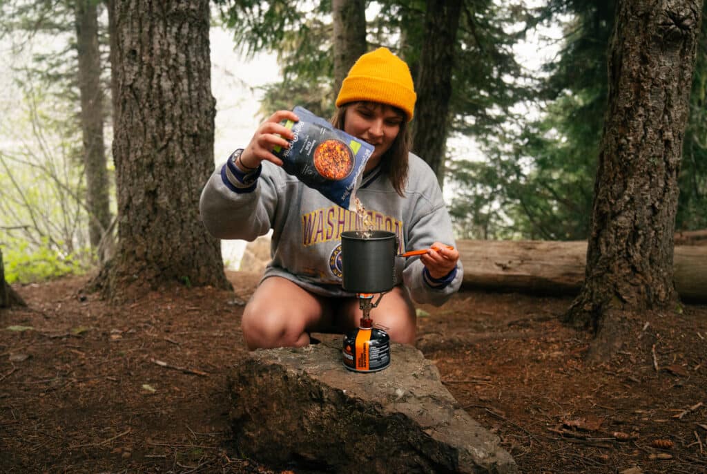A girl preparing a backpacking meal in a small pot at the Lake Angeles Campground.
