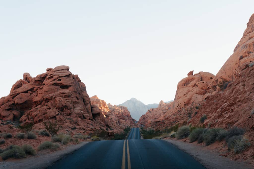A road that goes through Valley of Fire State Park, with rock formations surrounding it.