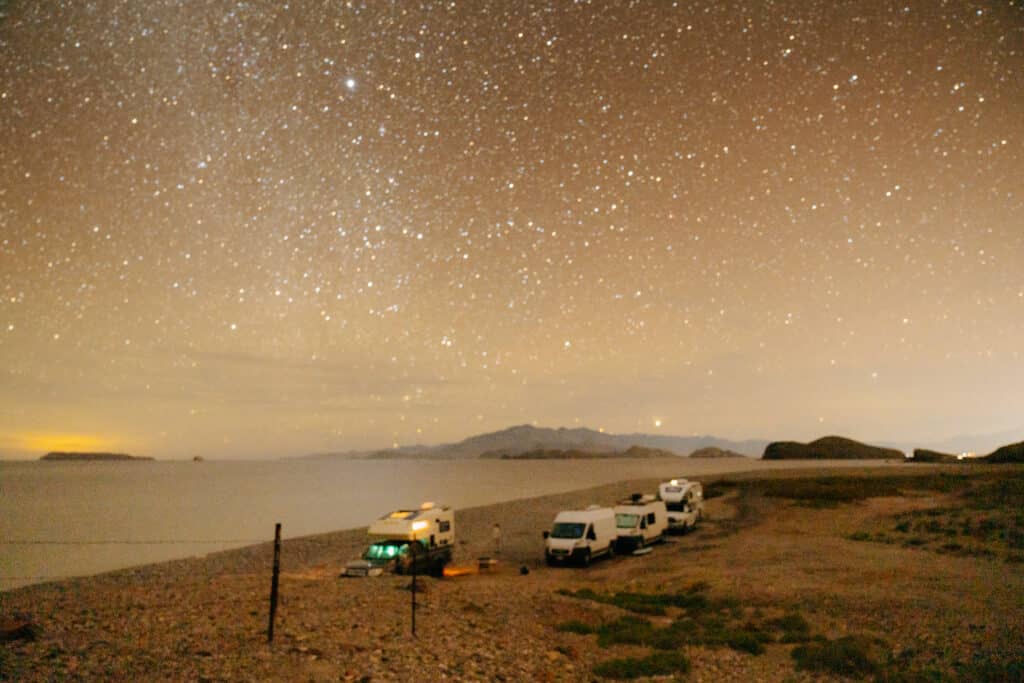 A night photo of four vans parked on a beach in Baja, with stars in the sky above them.