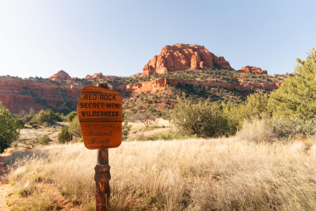 The beginning of the Bear Mountain trail in Sedona, with a sign that says "Red Rock Secret Mtn. Wilderness" in front of a red rock mountain.